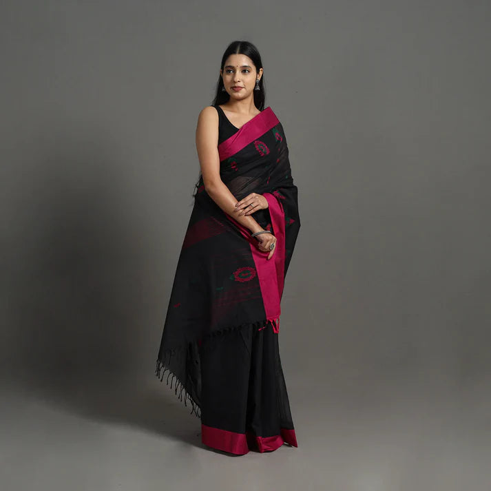 Plumvera model wearing black kanchipuram cotton saree with magenta border and pink floral motifs on neutral grey backdrop