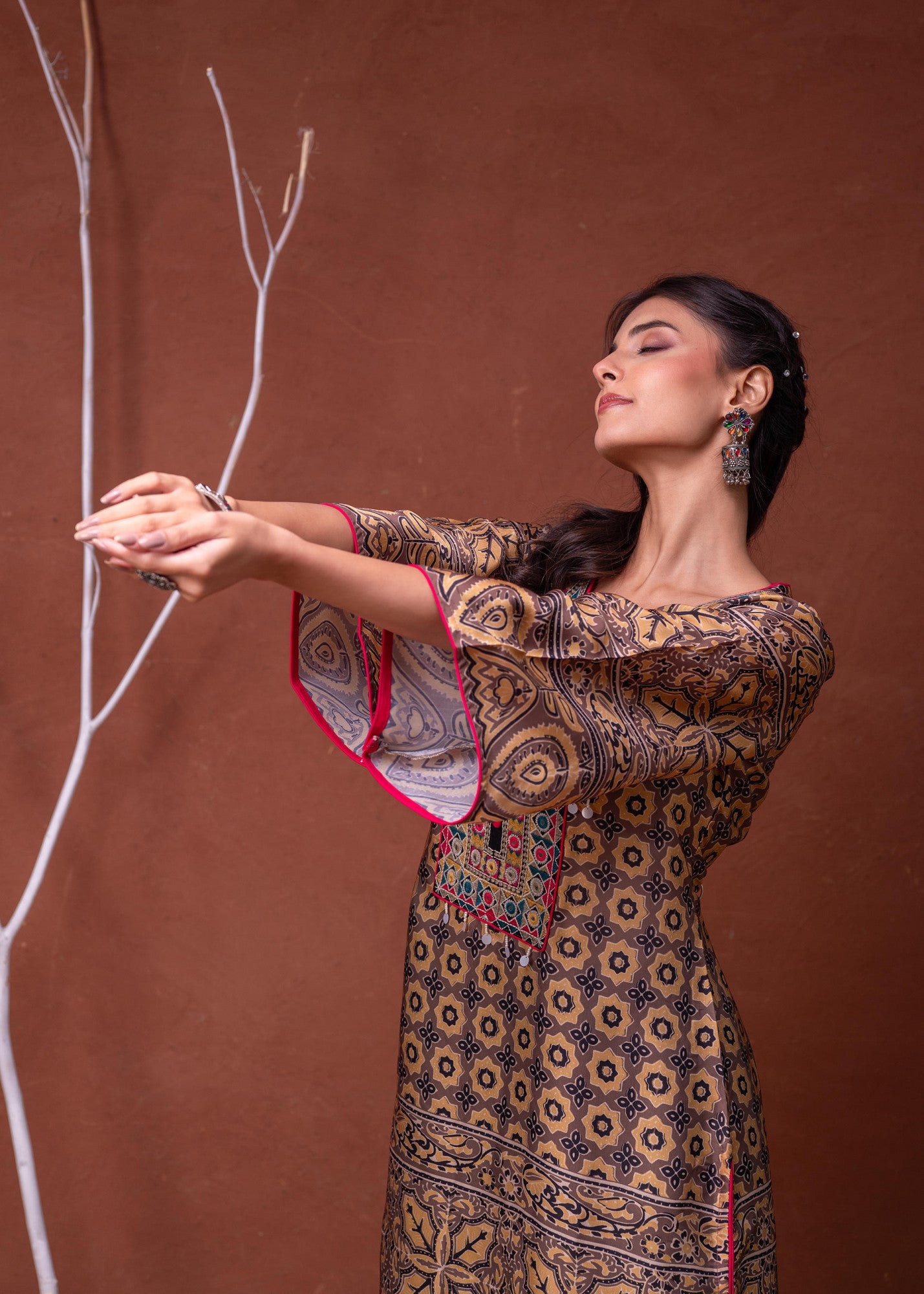 Model in mustard embroidered kurta pant set with floral print and pink trim bell sleeves posing against brown backdrop
