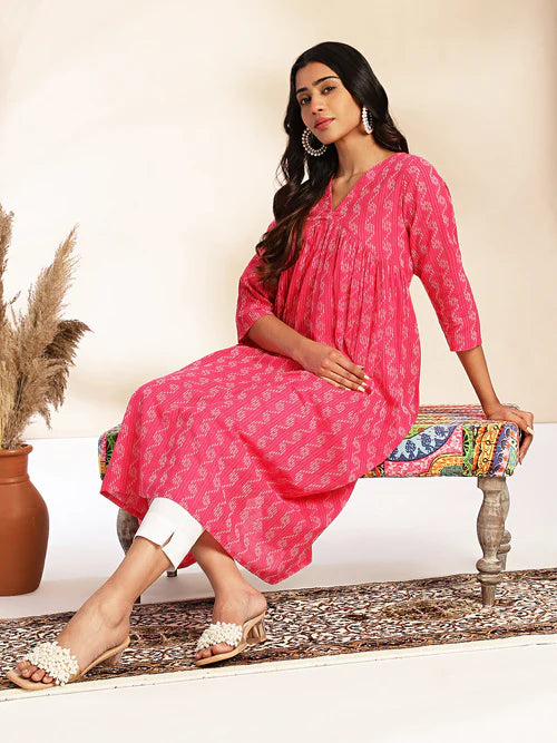 Model wearing pink cotton gathered kurta with white pants and sandals seated on decorative bench